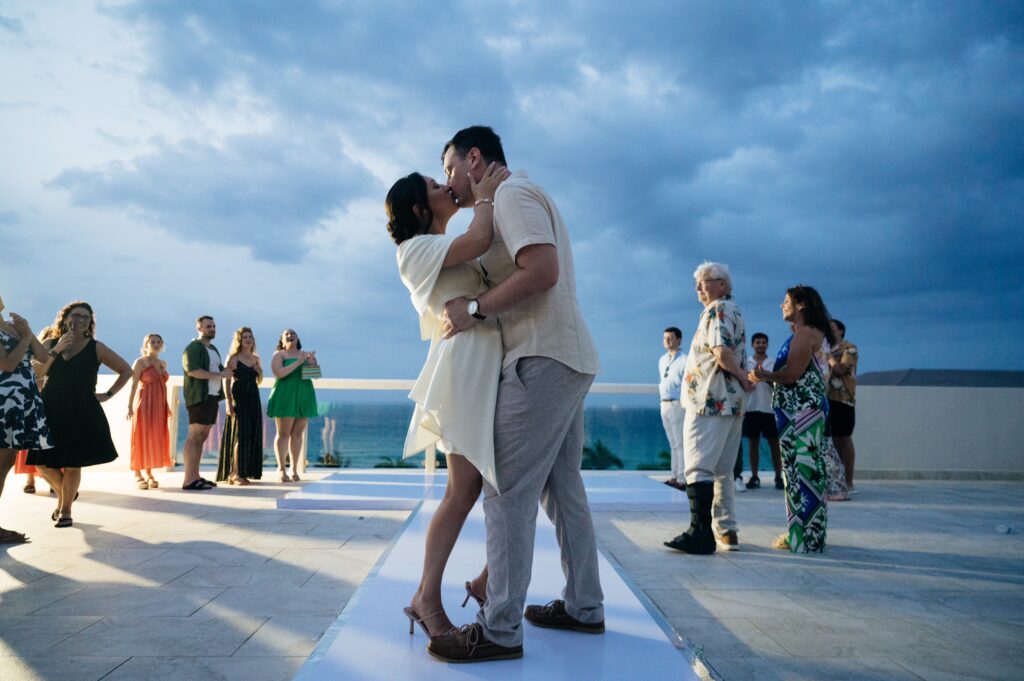 Bride and groom first dance on white terrace with ocean sunset backdrop