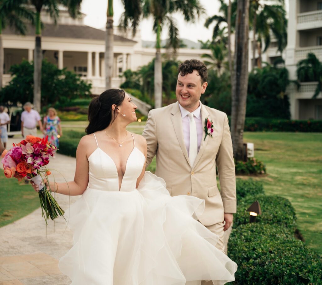 Candid wedding photo of a bride and groom at their destination wedding in Jamaica. The couple is walking and smiling after their ceremony, surrounded by palm trees.
