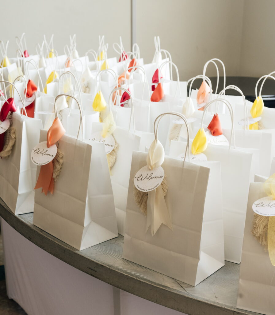 White gift bags with colorful tissue paper and welcome tags for wedding guests
